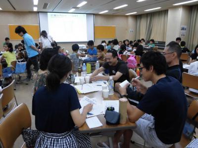 9月2日(日曜日)、町民会館で、親子参加型ワークショップ「発想力と決める力の育て方」が開催された際の各テーブルにて頭や手を動かし考える大人たちの画像