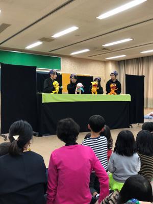 お楽しみ会で人形劇を見ている親子たちの様子の写真
