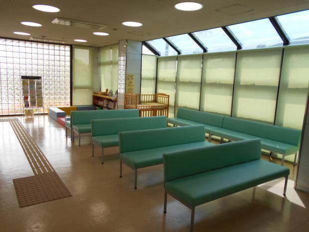 広い待合い室に緑色の長椅子が並べられている写真