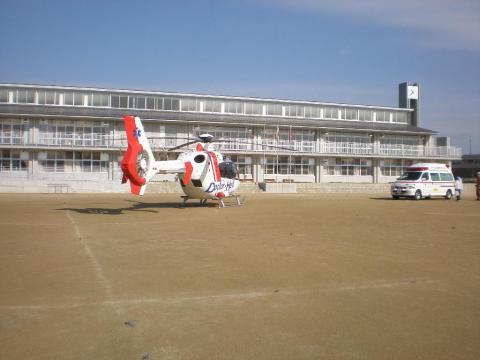 青空の下学校のグラウンドに着陸した1機のドクターヘリコプターの写真