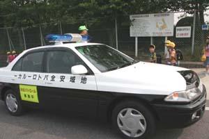 小学校前で小学生が数名と男性1名と青色パトロールカーが写っている写真