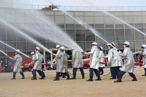 10人の消防隊員が同じ方向に斜め上に向かって水を放水している写真