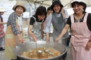 大きな鍋を囲んで炊き出しを行う4人の笑顔の女性たちの写真